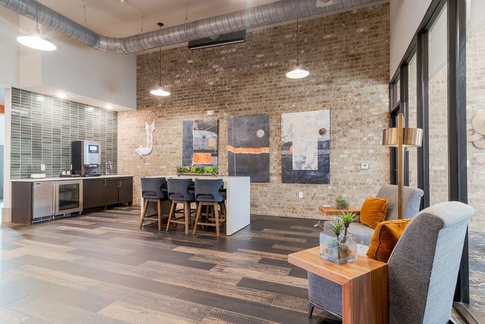 Chic modern lounge with industrial charm, featuring exposed brick walls, stylish artwork, and sleek seating by large windows.