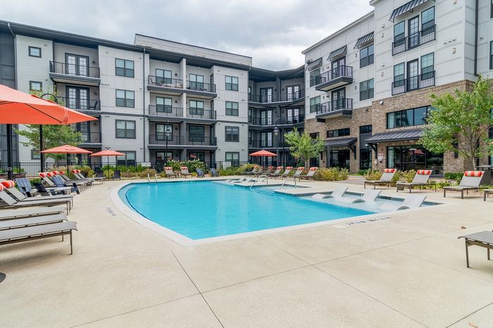 Luxurious apartment complex showcasing a sparkling pool with stylish lounge chairs and vibrant umbrellas, framed by modern architecture.