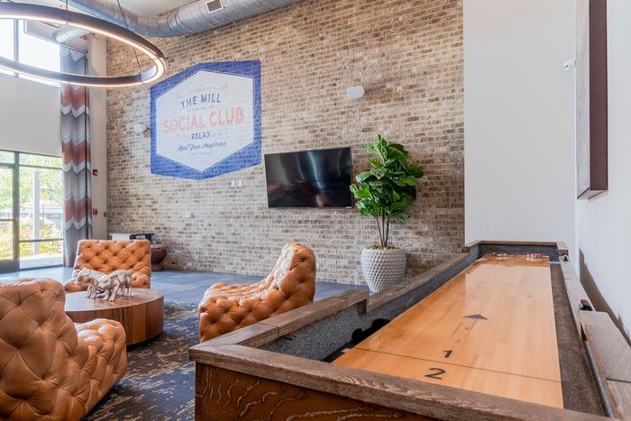 Inviting social club room with cozy orange tufted chairs, stylish decor, shuffleboard table, and a bright, welcoming ambiance.