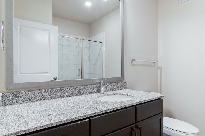 Elegant bathroom with modern granite countertop, sleek mirror, and spacious glass-enclosed shower.