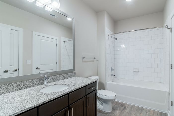 Modern bathroom featuring a sleek granite countertop, large mirror, and pristine white bathtub in a bright, inviting space.