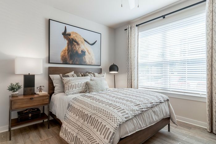 Cozy bedroom with modern decor, featuring a stylish wooden bed, patterned bedding, and an artistic Highland cow wall art.