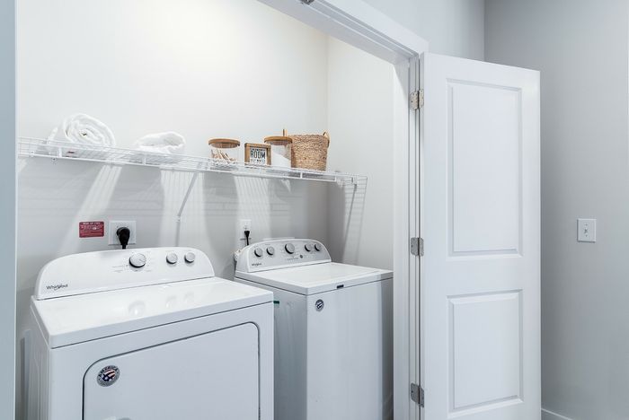 Bright laundry room with modern washing and drying machines, featuring organized shelving and cozy storage baskets.