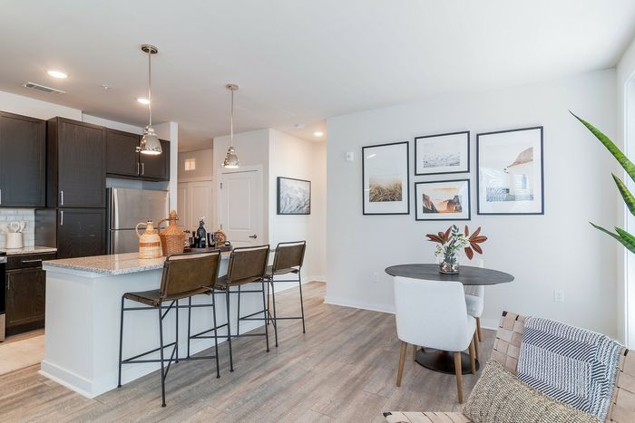Bright and modern kitchen with sleek dark cabinets, a polished granite island, and stylish pendant lighting, adjacent to a chic dining area with eye-catching artwork and cozy seating.