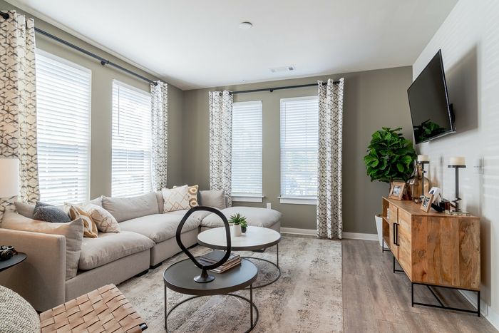 Bright and inviting living room featuring a sleek sectional sofa, modern coffee tables, flat-screen TV, and a wooden media console accented by lush greenery.