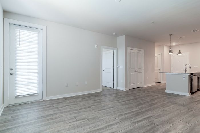 Bright and modern open-concept apartment with sleek wood flooring, large windows, and a stylish kitchen with pendant lighting and granite countertops.