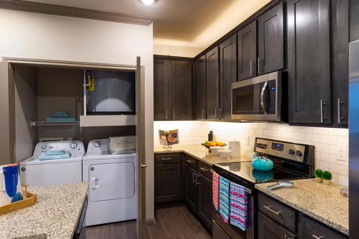 Modern kitchen with sleek dark cabinetry, stainless steel appliances, and convenient in-unit laundry setup.
