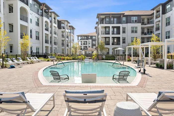 Inviting residential complex with modern architecture surrounding a sparkling pool and elegant sun loungers, perfect for relaxation and leisure.