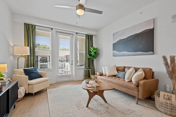 Bright and inviting living room with modern decor, featuring a stylish tan sofa, elegant armchair, and abundant natural light through large windows.
