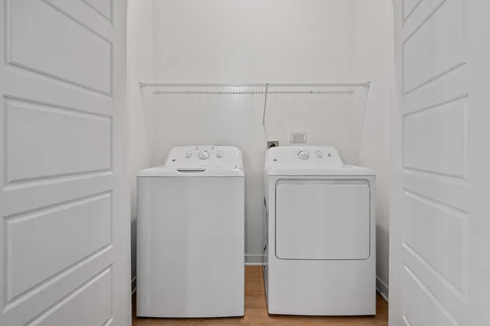 Bright laundry room featuring modern washer and dryer with sleek white design and wooden floors.