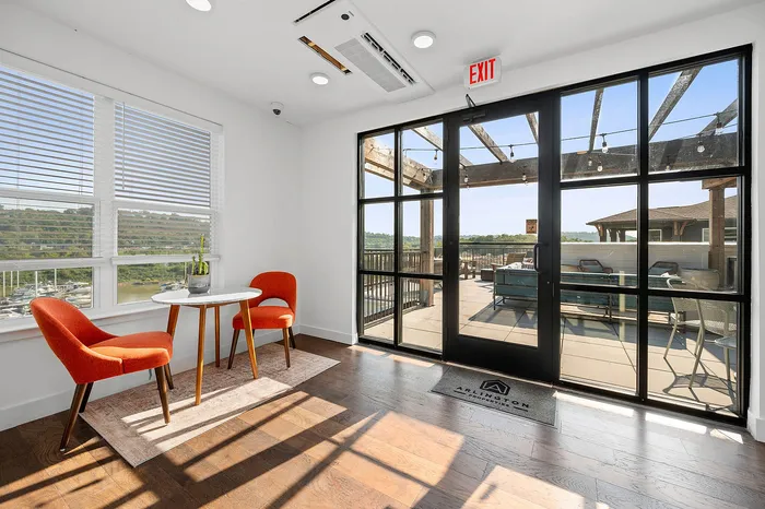 Bright and inviting space with a seating area featuring vibrant orange chairs and a stunning view through large windows leading to a spacious patio.