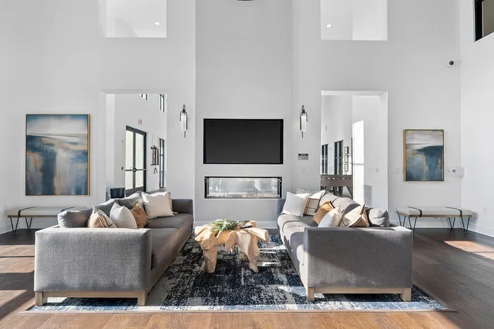 Elegant modern living room with high ceilings, featuring stylish grey sofas, a unique wooden coffee table, and contemporary artwork enhancing natural light.