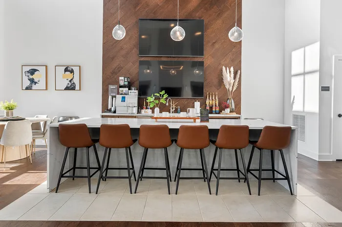 Elegant kitchen with modern design featuring a sleek marble island, six stylish brown barstools, dual TVs, and decorative artwork.