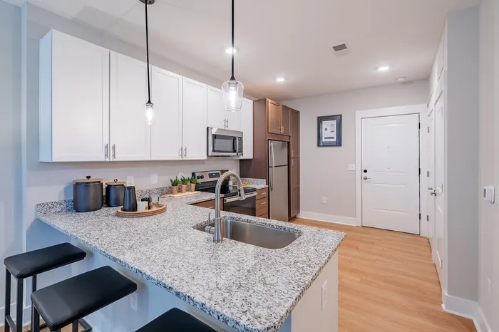 Modern kitchen with granite countertop, stylish pendant lighting, and stainless steel appliances, offering ample storage and seating.