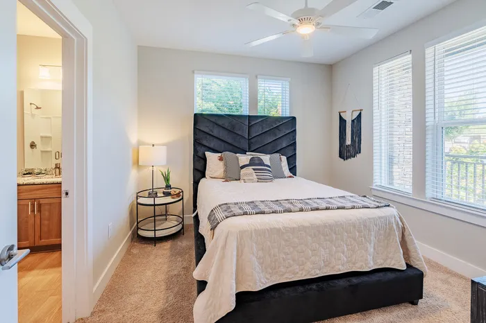 Bright and inviting bedroom featuring a plush bed with elegant bedding, natural light streaming through large windows, and a stylish side table with decor.
