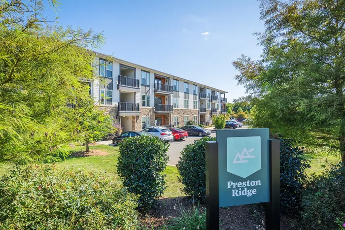 Charming three-story apartment complex surrounded by lush greenery, featuring modern balconies and ample parking at Preston Ridge.