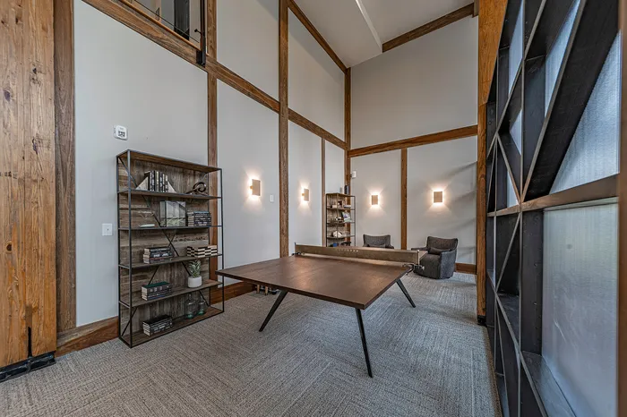 Modern loft-style room with high ceilings, featuring a sleek wooden table, stylish shelving, and cozy seating, offering a sophisticated yet inviting ambiance.