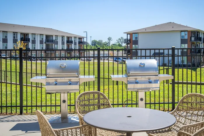 Chic outdoor patio with sleek stainless steel grills and cozy wicker chairs, offering a perfect space for gatherings in an upscale apartment community.