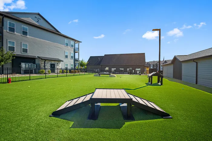 Beautifully landscaped communal area featuring lush green lawns, a modern apartment building, and a cozy seating area under a clear blue sky.