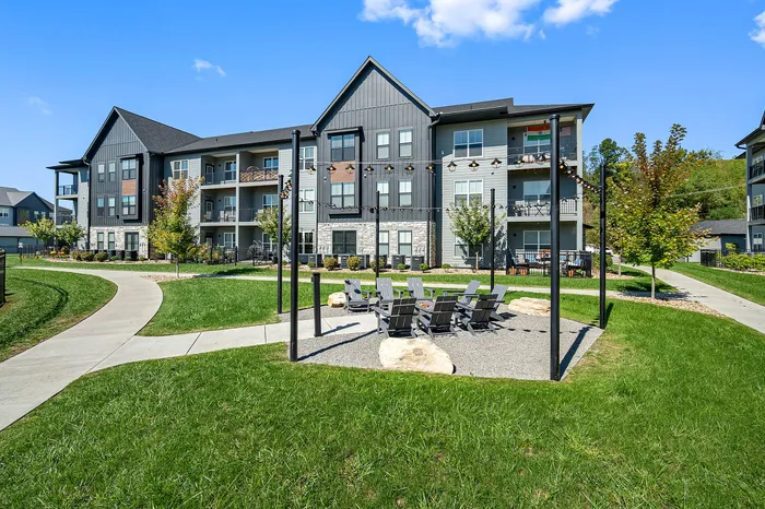 Charming apartment complex with modern design, highlighted by lush green landscaping and inviting outdoor seating area under string lights.