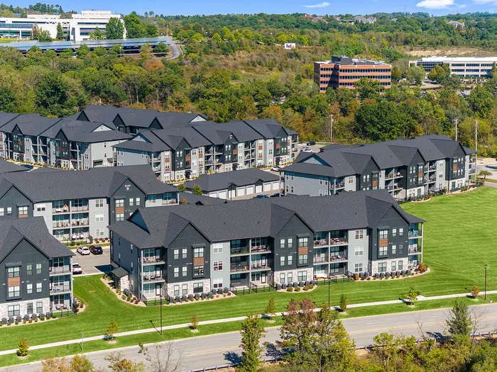Inviting aerial view of modern apartment complex nestled in lush greenery, boasting spacious balconies and a serene neighborhood setting.