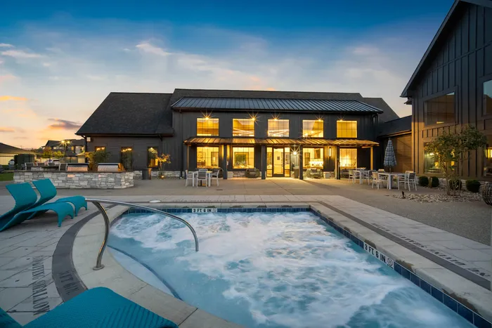 Luxurious modern clubhouse with illuminated interiors, surrounded by comfortable outdoor seating and a bubbling jacuzzi, set against a stunning evening sky.