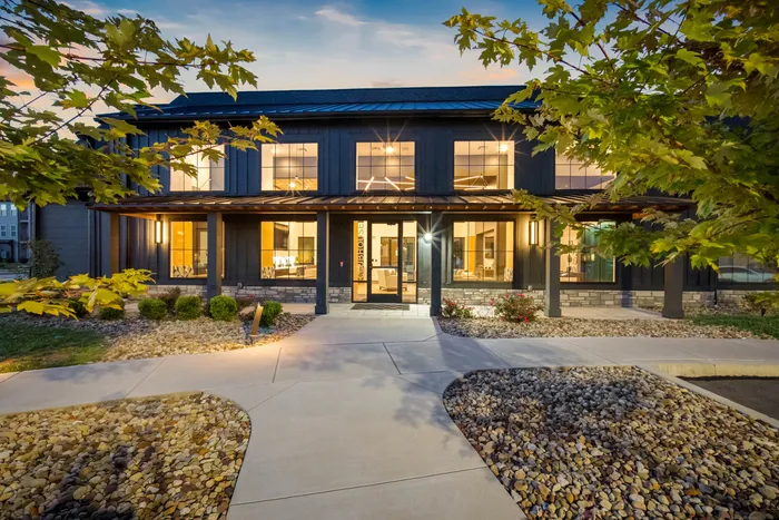Charming modern building exterior with warm lighting and lush landscaping, inviting ambiance at dusk.