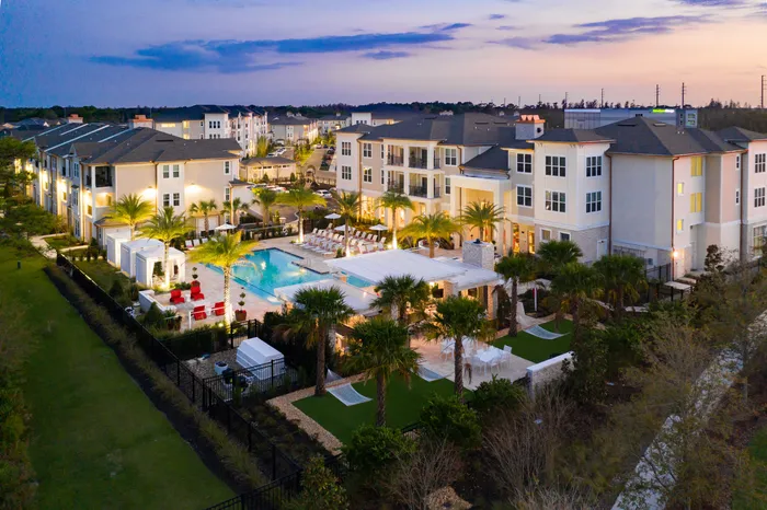 Elegant apartment complex at dusk showcasing a spacious outdoor pool area, lush palm trees, and stylish cabanas for a luxurious lifestyle.