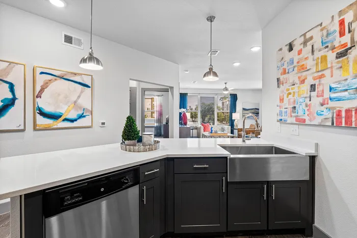Modern apartment kitchen with sleek countertops, stainless steel sink, and contemporary artwork, flowing into a bright living room with stylish decor and large windows.