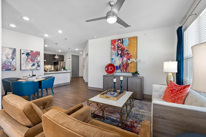 Elegant open-plan living area with modern decor, featuring a cozy seating arrangement, vibrant artwork, and stylish dining space leading to a sleek kitchen.