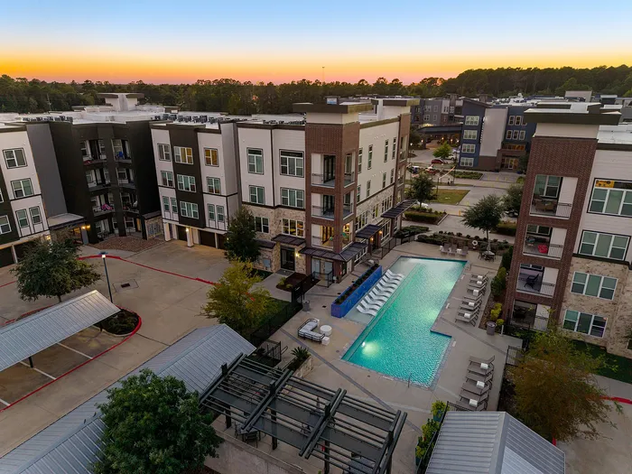 Elegant aerial view of a modern apartment complex featuring a stunning outdoor pool area surrounded by stylish seating, set against a serene sunset backdrop.
