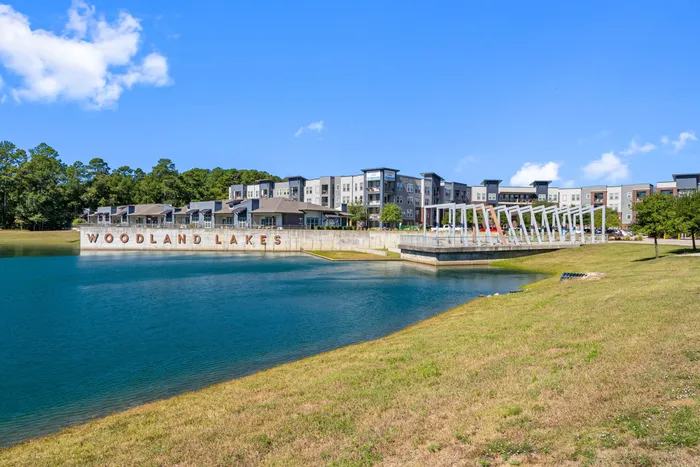Charming apartment complex by Woodland Lakes with modern architecture, surrounded by lush greenery and a serene water feature.