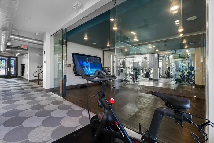 Modern apartment gym with sleek Peloton bike and stylish glass wall design, offering a bright and inviting fitness space.