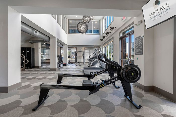 Modern fitness center with rowing machines, spacious interior, high ceilings, and vibrant natural light at Enclave at Woodland Lakes.