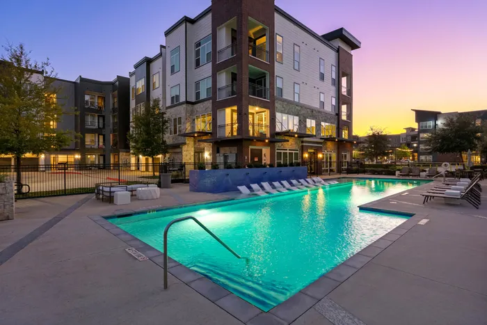 Chic apartment complex featuring a vibrant pool area with lounge chairs, surrounded by modern architecture at sunset.