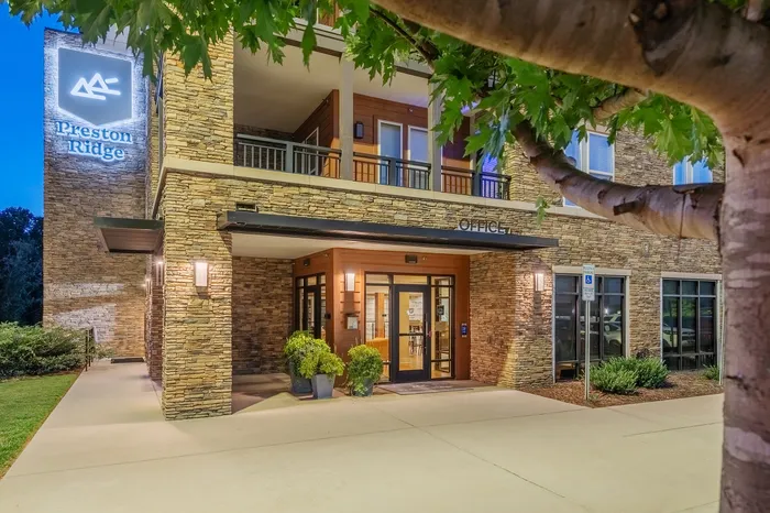 Inviting exterior view of Preston Ridge with beautiful stone facade and lush greenery, highlighting the welcoming office entrance.