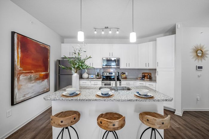Bright, modern kitchen featuring sleek white cabinets, stainless steel appliances, and a stylish granite island with unique wood stools.