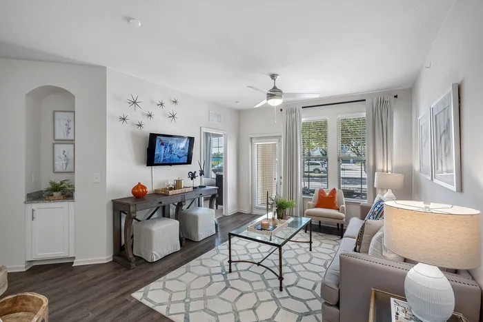 Chic and inviting living room with modern decor, featuring a wall-mounted TV, stylish furniture, and abundant natural light from large windows.