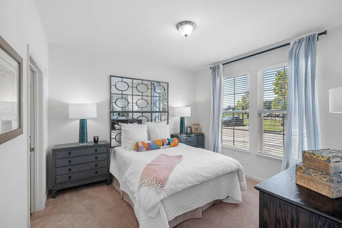 Bright and welcoming bedroom with cozy decor, large mirrored headboard, and sunlit windows offering a serene view.