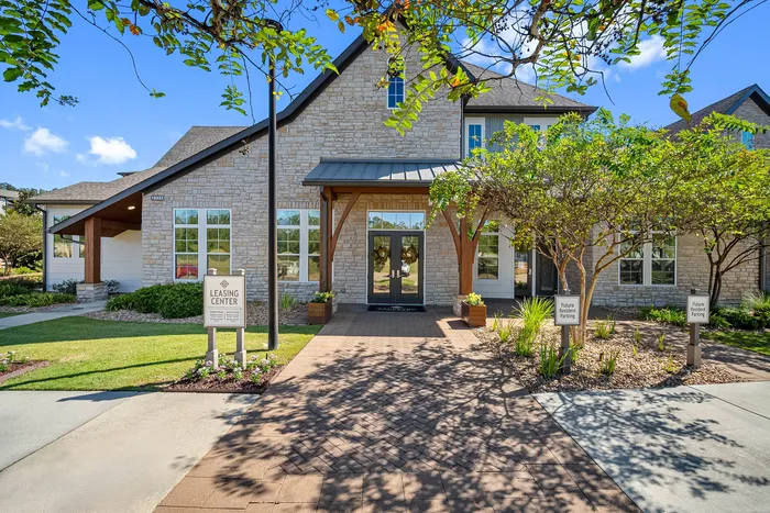 Charming apartment leasing center with rustic stonework, surrounded by lush greenery and a welcoming path.