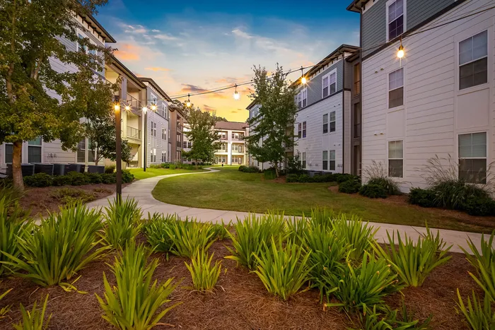 Charming apartment complex with beautifully landscaped gardens, cozy lighting, and a serene pathway at sunset.