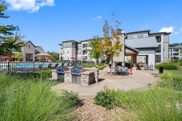 Inviting apartment complex with modern architecture, poolside lounging area, and outdoor grilling stations amidst lush landscaping.