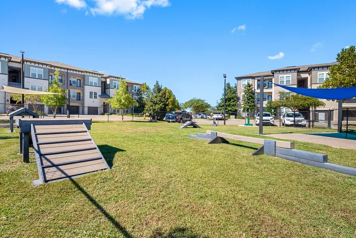 Modern apartment complex with beautiful landscape, featuring a well-maintained green space and recreational area under a bright blue sky.
