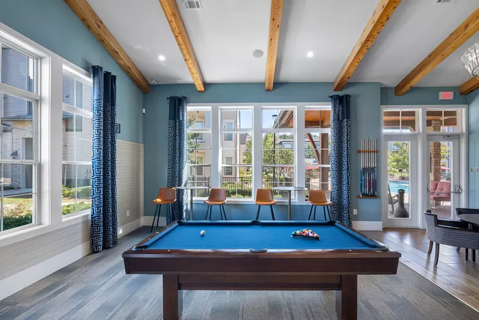 Bright and inviting recreation room featuring a sleek pool table, modern decor, and large windows with pool views.