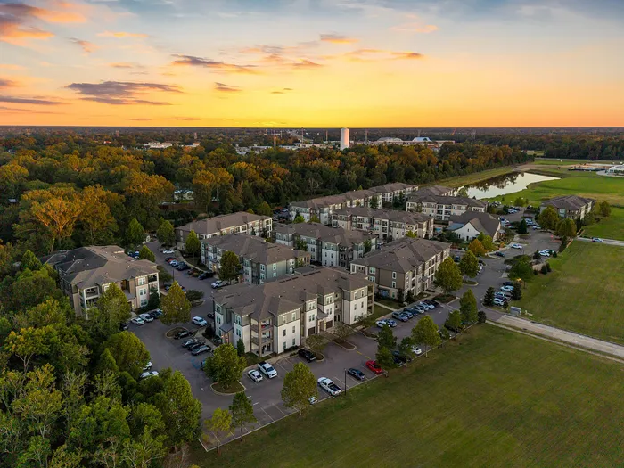 Picturesque aerial view of a charming apartment complex surrounded by lush greenery at sunset, offering serene living with ample parking and beautiful landscapes.