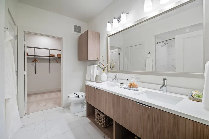 Elegant modern bathroom with dual sinks, sleek wooden cabinetry, and a spacious walk-in closet.
