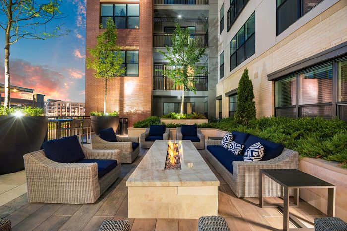Luxurious outdoor patio at sunset featuring elegant wicker seating around a stylish fire pit, surrounded by lush greenery.