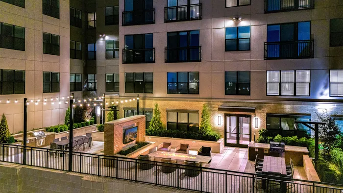 Elegant apartment courtyard at night featuring cozy seating, a modern fire pit, and ambient string lighting, perfect for outdoor gatherings.