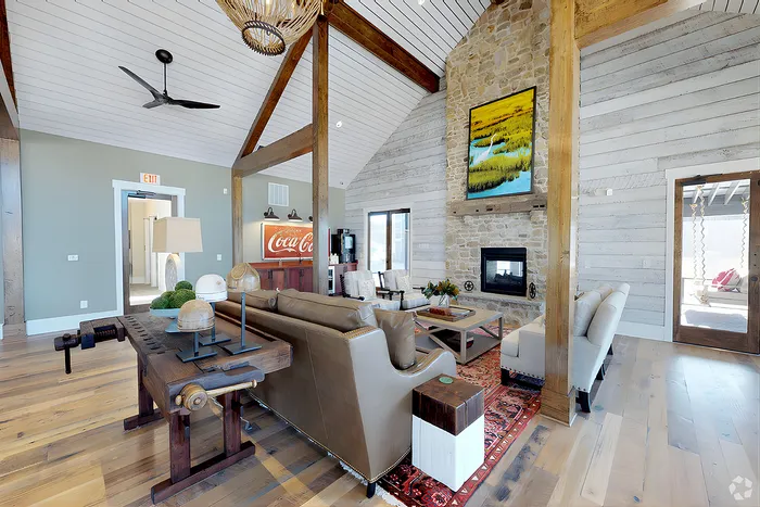Charming club room with rustic elegance, featuring a cozy stone fireplace, vaulted ceiling with exposed beams, and stylish modern lighting.