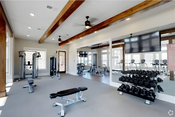 Modern fitness center featuring state-of-the-art exercise equipment, bright windows, and stylish wooden beams.